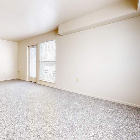 Thumbnail 3 of 8 An enlarged living room with a carpeted floor and a door leading to a patio at Gull Prairie/Gull Run Apartments and Townhomes, Kalamazoo, 49048