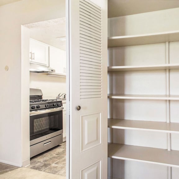 Thumbnail 6 of 9 a pantry with white shelving and a kitchen with a stove and at Hickory Village Apartments, Indiana