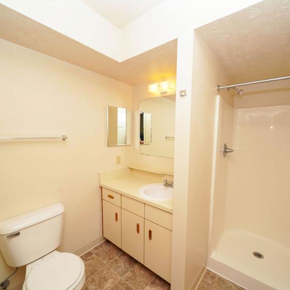 Thumbnail 9 of 9 A toilet, sink, and mirror sits next to a shower in a bathroom at The Highlands Apartments in Elkhart, IN