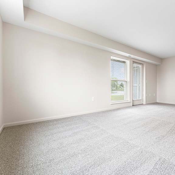 Thumbnail 5 of 12 A spacious living room with a carpeted floor and a french door to a patio at Hunters Pond Apartment Homes, Champaign, IL