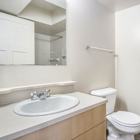 Thumbnail 11 of 16 A primary bathroom with a toilet, sink, and a mirror at Indian Lakes Apartments, Mishawaka, IN