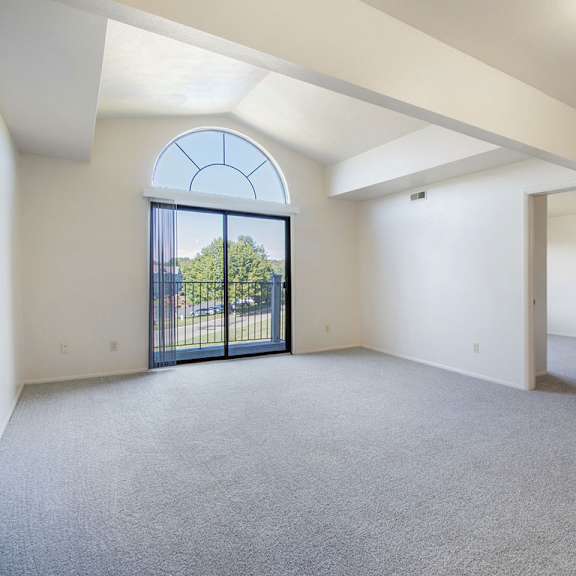 Thumbnail 4 of 10 A spacious living room with a cathedral ceiling, large arched window and a carpeted floor at Liberty Mills Apartments, Fort Wayne