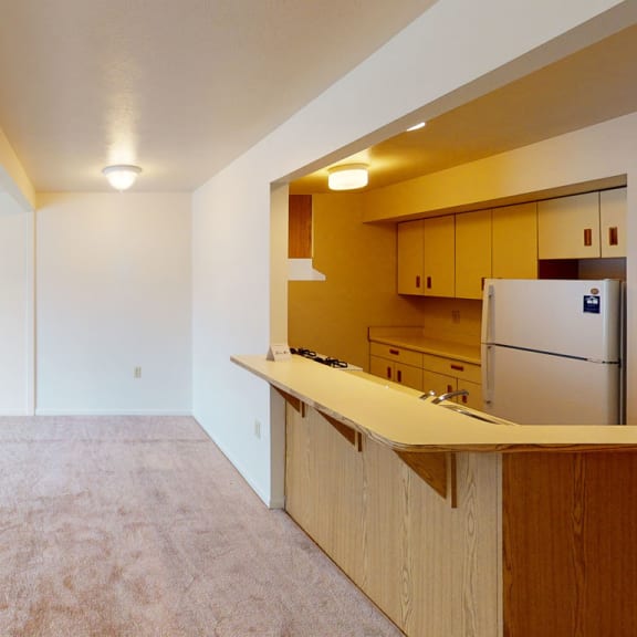 Thumbnail 5 of 12 an empty living room with a kitchen and a refrigerator