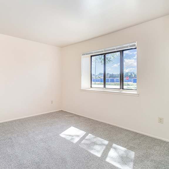 Thumbnail 12 of 14 A bedroom with a large window and a carpeted floor at Mount Royal Townhomes in Kalamazoo, MI