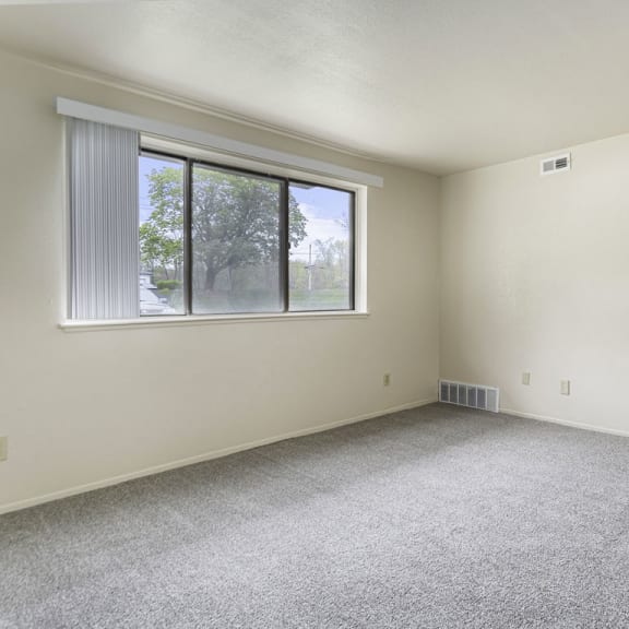 Thumbnail 6 of 19 a garden style living room with a large window and carpeting at Normandy Village Apartments, Michigan City, IN