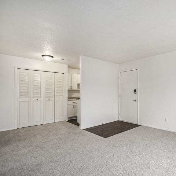 Thumbnail 7 of 19 an empty living room and kitchen with white walls and carpet at Normandy Village Apartments, Michigan City, IN