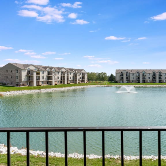 Thumbnail 4 of 11 a pond with a fountain in front of an apartment building  at Oak Shores Apartments, Oak Creek, WI, 53154