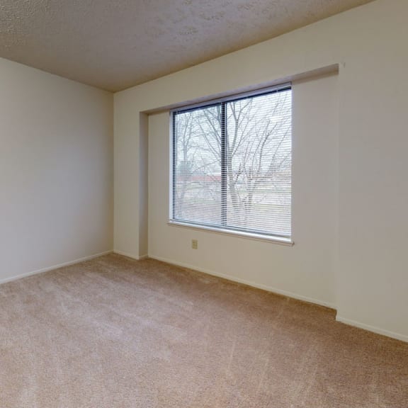 Thumbnail 6 of 7 a bedroom with a large window and beige carpeting at Pine Knoll Apartments, Battle Creek, MI