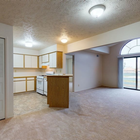 Thumbnail 3 of 7 an empty living room with a kitchen and a glass door  at Pine Knoll Apartments, Battle Creek, Michigan