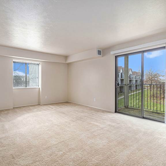 Thumbnail 4 of 9 An enlarged living room with a carpeted floor, a sliding glass door, and a window at Pine Knoll Apartments, Battle Creek, MI