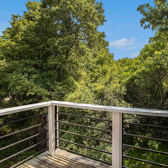 Thumbnail 4 of 17 A balcony with a metal railing overlooks a wooded area at Pine Knoll Apartments, Battle Creek, 49014