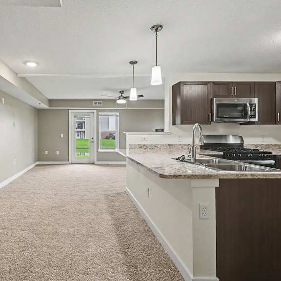 Thumbnail 3 of 12 A kitchen with a breakfast bar and a carpeted dining room at The Reserve at The Reserve at Destination Pointe in Grimes, IA 50111