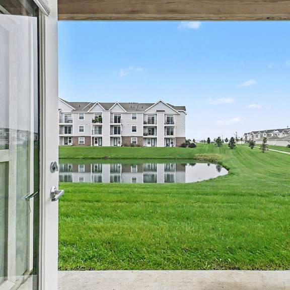 Thumbnail 4 of 12 A view of a grassy area from a patio with a building in the background at The Reserve at The Reserve at Destination Pointe in Grimes, IA 50111