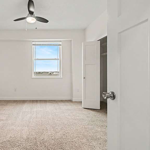 Thumbnail 15 of 16 A spacious bedroom with a carpeted floor, a ceiling fan, and a window with a view at The Reserve at The Reserve at Destination Pointe in Grimes, IA 50111