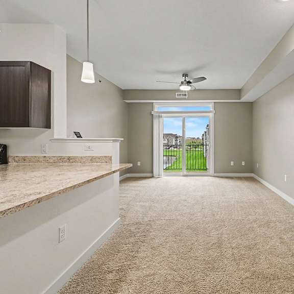 Thumbnail 3 of 16 A spacious living and dining room with a carpeted floor and a ceiling fan at The Reserve at The Reserve at Destination Pointe in Grimes, IA 50111