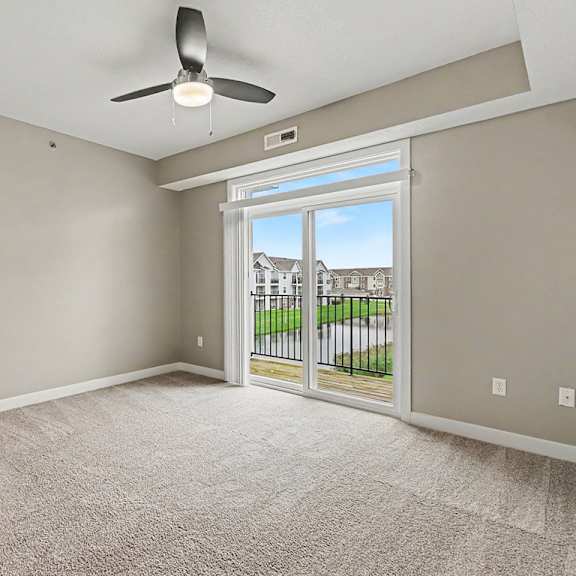 Thumbnail 4 of 16 A living room with a 9 foot ceiling, ceiling fan and a sliding glass door leading to a balcony at The Reserve at The Reserve at Destination Pointe in Grimes, IA 50111