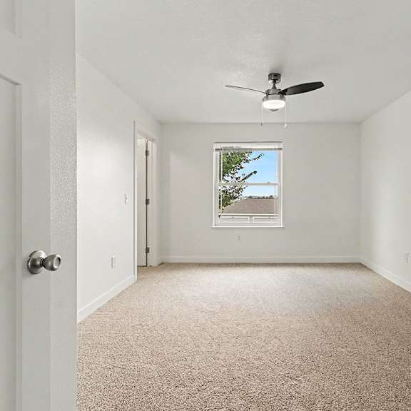 Thumbnail 12 of 16 A large bedroom with a carpet floor and a ceiling fan at The Reserve at The Reserve at Destination Pointe in Grimes, IA 50111