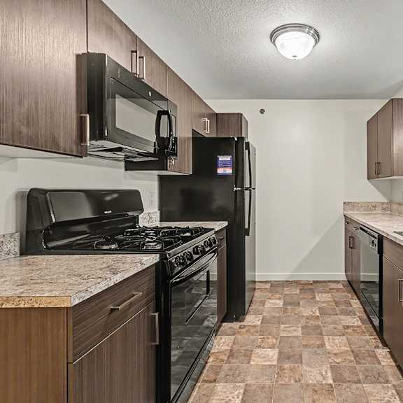 Thumbnail 7 of 16 A kitchen with black appliances and brown cabinets at The Reserve at The Reserve at Destination Pointe in Grimes, IA 50111