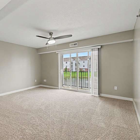 Thumbnail 4 of 16 A living room with a carpeted floor and a ceiling fan leading to a balcony at The Reserve at The Reserve at Destination Pointe in Grimes, IA 50111