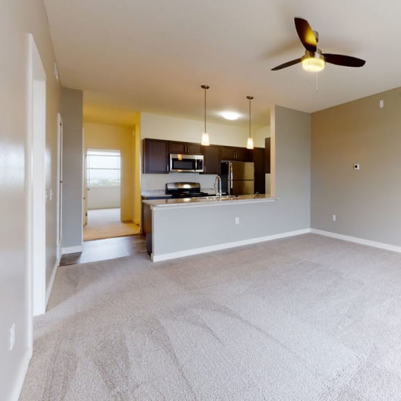Thumbnail 4 of 10 an empty living room and kitchen with a ceiling fan at The Reserve at Destination Pointe, Grimes, IA, 50111
