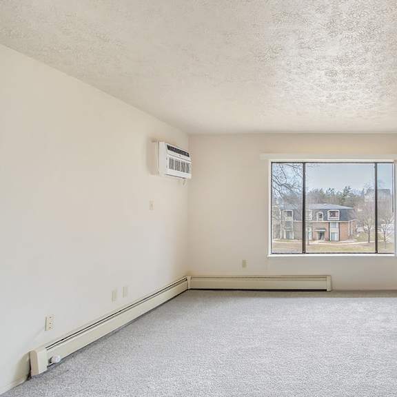 Thumbnail 10 of 13 A spacious living room with a window and a carpeted floor at Seville Apartments, Michigan