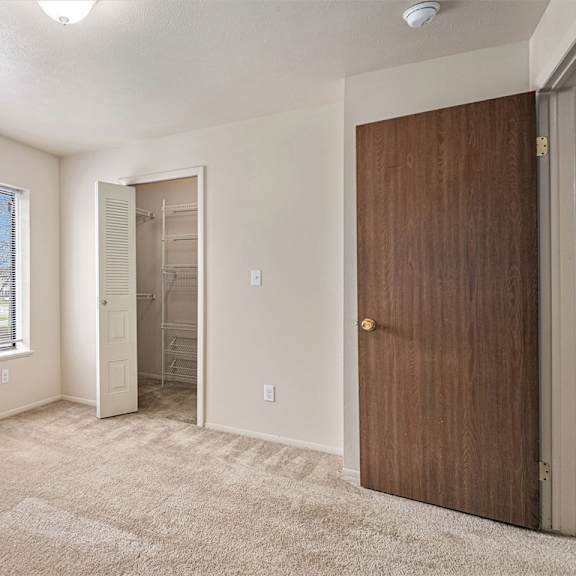 Thumbnail 24 of 24 A room with a brown door, a window with a view of a tree-lined street, and a carpeted floor.