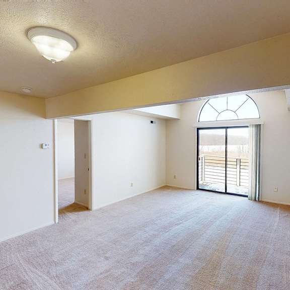 Thumbnail 3 of 8 A spacious living room with a carpeted floor and a cathedral ceiling with a large window at South Bridge Apartments, Fort Wayne, Indiana