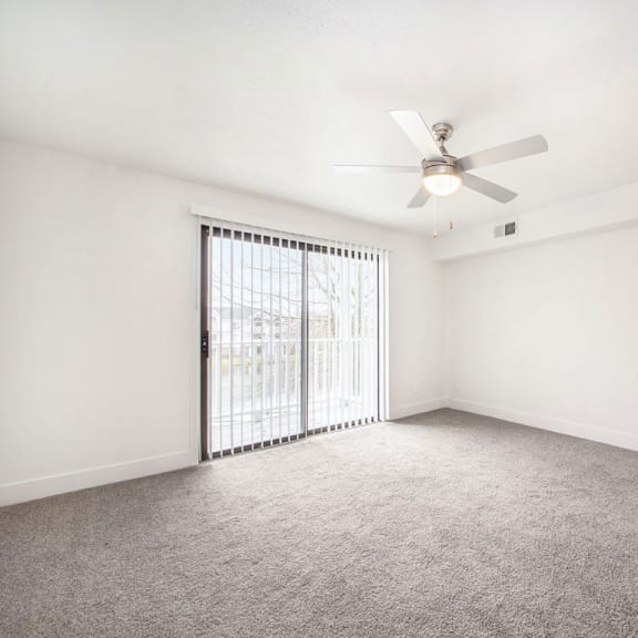 Thumbnail 4 of 10 an empty living room with a ceiling fan and a slider to a private balcony at Stoney Pointe Apartment Homes, Wichita, 67226