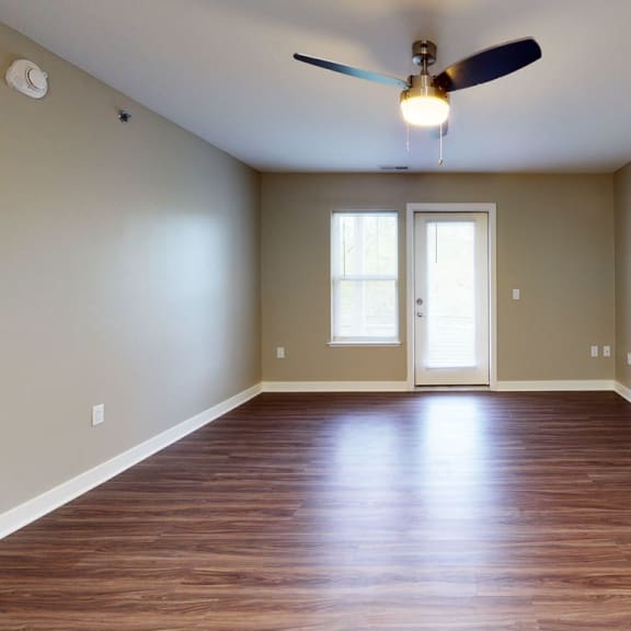 Thumbnail 4 of 14 an empty living room with hard surface floors and a ceiling fan at Strathmore Apartment Homes, Iowa
