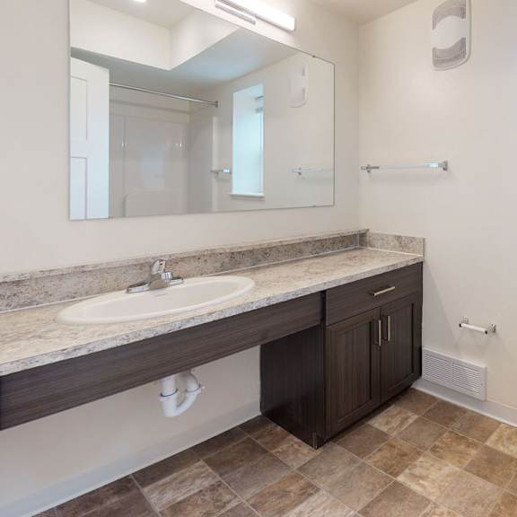 Thumbnail 6 of 8 A bathroom with a window, toilet, sink, and mirror at Strathmore Apartment Homes in West Des Moines, IA