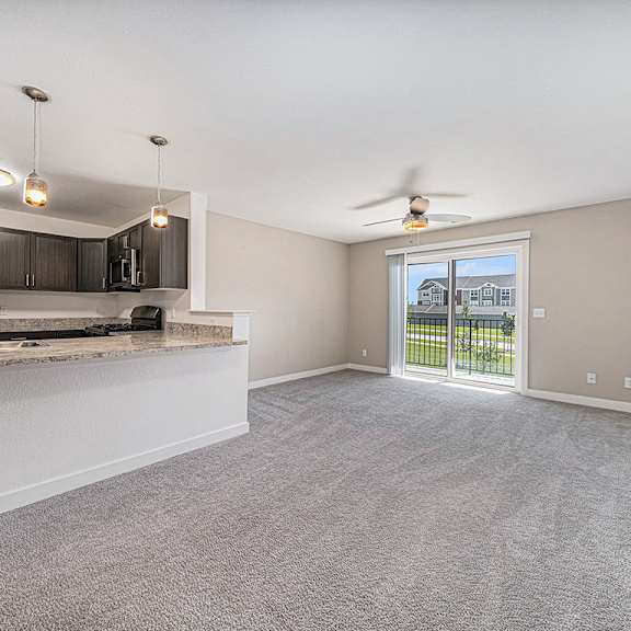 Thumbnail 3 of 9 A spacious living room with a kitchen area and sliding glass doors leading to a balcony at Strathmore Apartment Homes in West Des Moines, IA