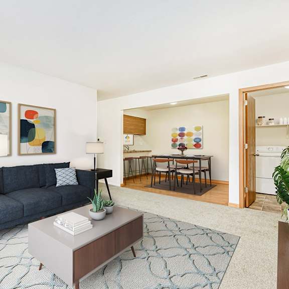 Thumbnail 7 of 19 Living and dining rooms with a couch, a coffee table, and a laundry room  at Tanglewood Apartments, Oak Creek, WI
