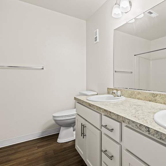 Thumbnail 15 of 19 An ensuite bathroom with a toilet, two sinks, and mirror at Tanglewood Apartments, Oak Creek, WI