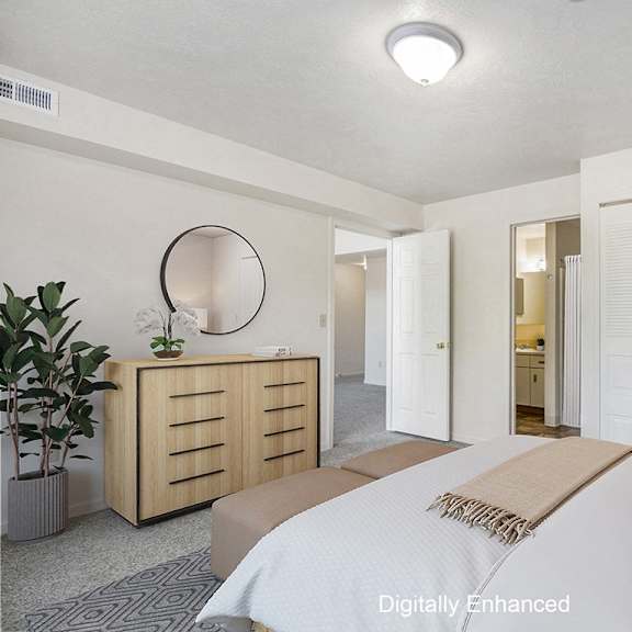 Thumbnail 12 of 13 A bedroom with an ensuite, a bed, nightstand, and a plant at The Highlands Apartments, Elkhart
