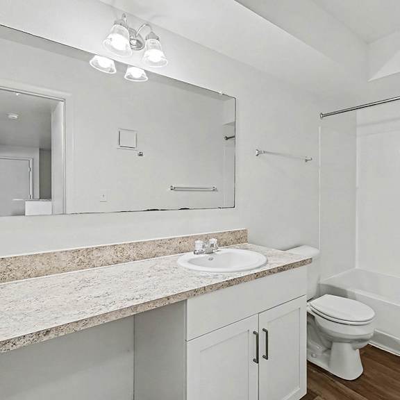 Thumbnail 10 of 11 A white bathroom with a sink, mirror, and bathtub at Trappers Cove Apartments, Lansing