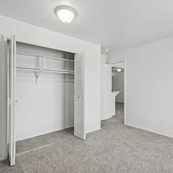 Thumbnail 12 of 12 A white bedroom with a closet and plush carpeting at Trappers Cove Apartments, Lansing