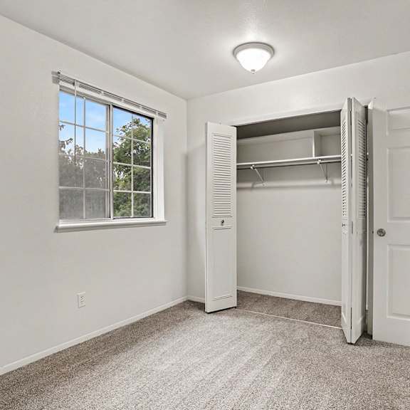 Thumbnail 11 of 11 A white bedroom with a window and a closet at Walnut Trail Apartments, Michigan