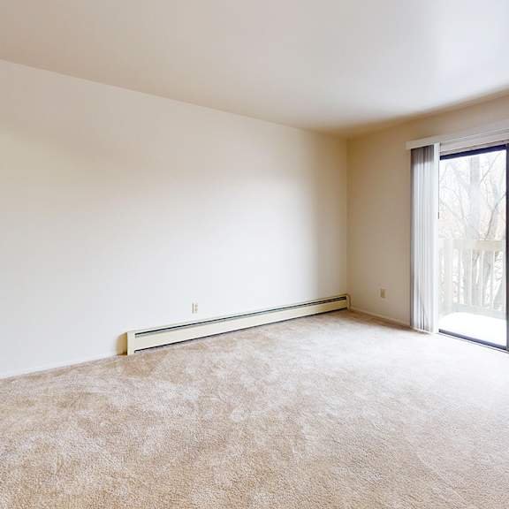 Thumbnail 3 of 11 A living room with a carpeted floor and a sliding glass door to a balcony at Waverly Park Apartments, Lansing