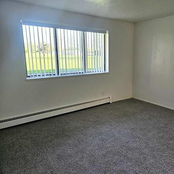 Thumbnail 3 of 15 A living room with a garden window and carpeted floor at Waverly Park Apartments, Lansing
