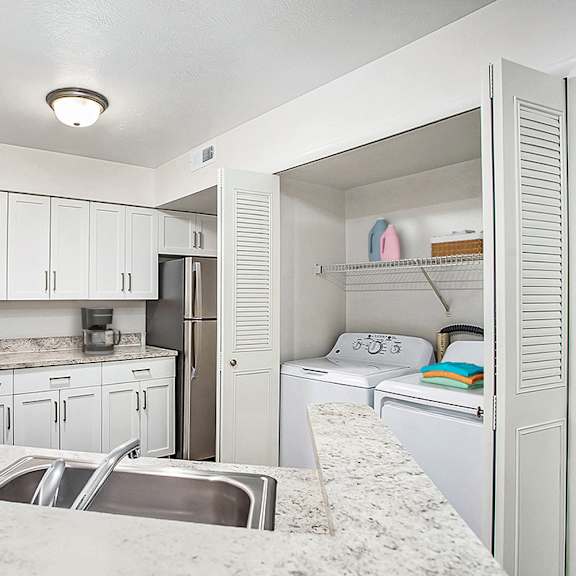 Thumbnail 12 of 17 A kitchen with white cabinets and a full size washer and dryer at West Hampton Park Apartments in Elkhorn, NE 68022