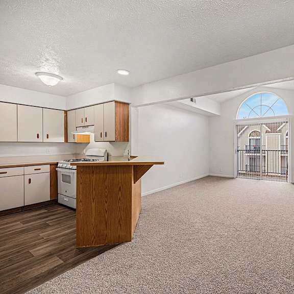 Thumbnail 5 of 17 A kitchen with white appliances and wooden cabinets along with a living room with a cathedral ceiling  at West Hampton Park Apartment Homes, Nebraska, 68022