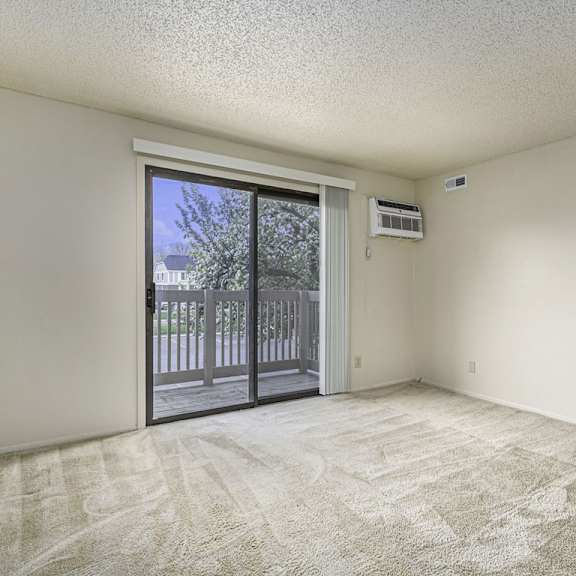 Thumbnail 4 of 10 A living room with a carpeted floor and a sliding glass door leading to a balcony at West Wind Apartments, Fort Wayne, 46808