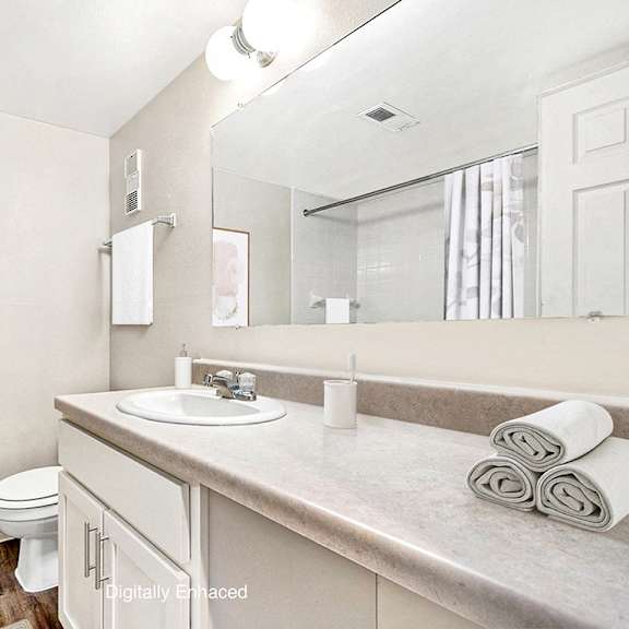 Thumbnail 7 of 11 A bathroom with a toilet, sink, and mirror at West Wind Apartments, Indiana, 46808