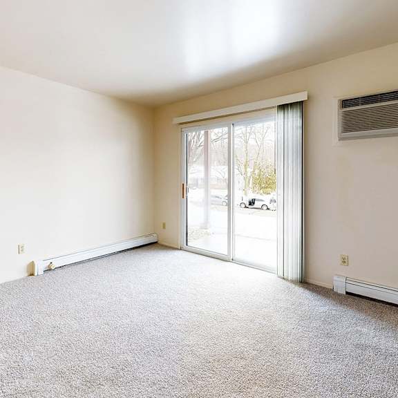 Thumbnail 4 of 8 A living room with a carpeted floor, sliding glass doors, and a window with blinds at Wood Creek Apartments, Kenosha, WI, 53144