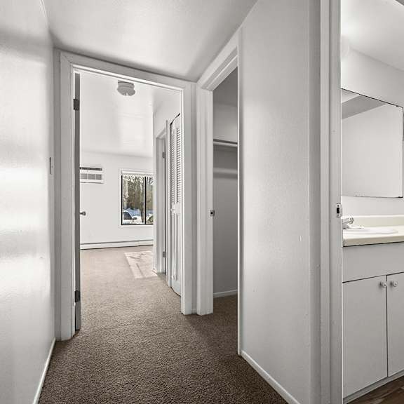 Thumbnail 6 of 14 A hallway looking into a bathroom with a sink, mirror, and toilet at Wood Creek Apartments, Kenosha