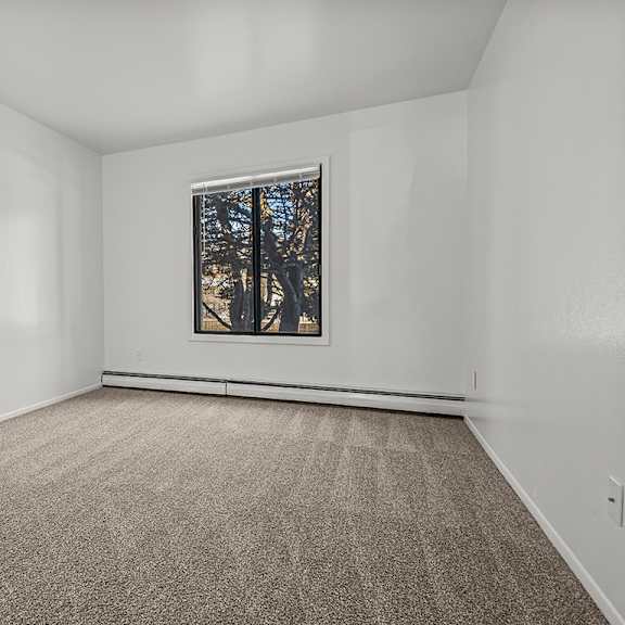 Thumbnail 9 of 14 A bedroom with a carpeted floor and a window showing trees outside at Wood Creek Apartments, Kenosha