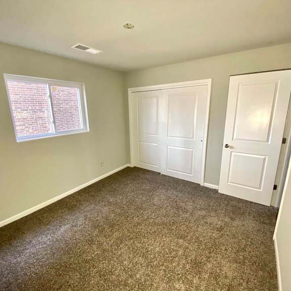 a room with carpeted floor, two doors, and a window with blinds.