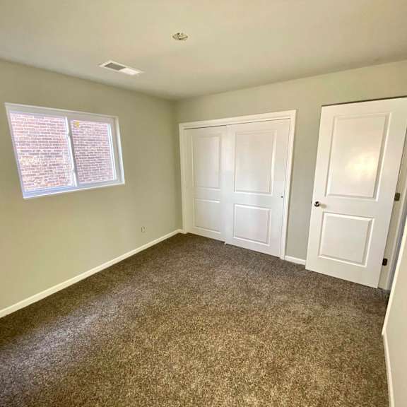 a room with carpeted floor, two doors, and a window with blinds.
