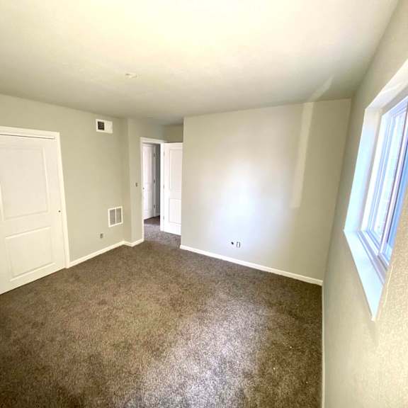a room with carpeted floor, two doors, and a window.