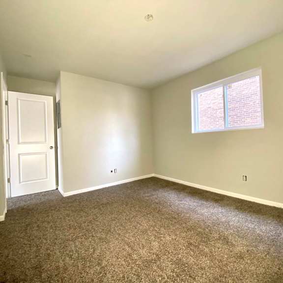 a room with a carpeted floor, a door, and a window with blinds.